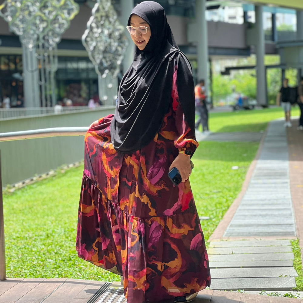 Woman in a colorful dress and black hijab standing outdoors on a pathway.